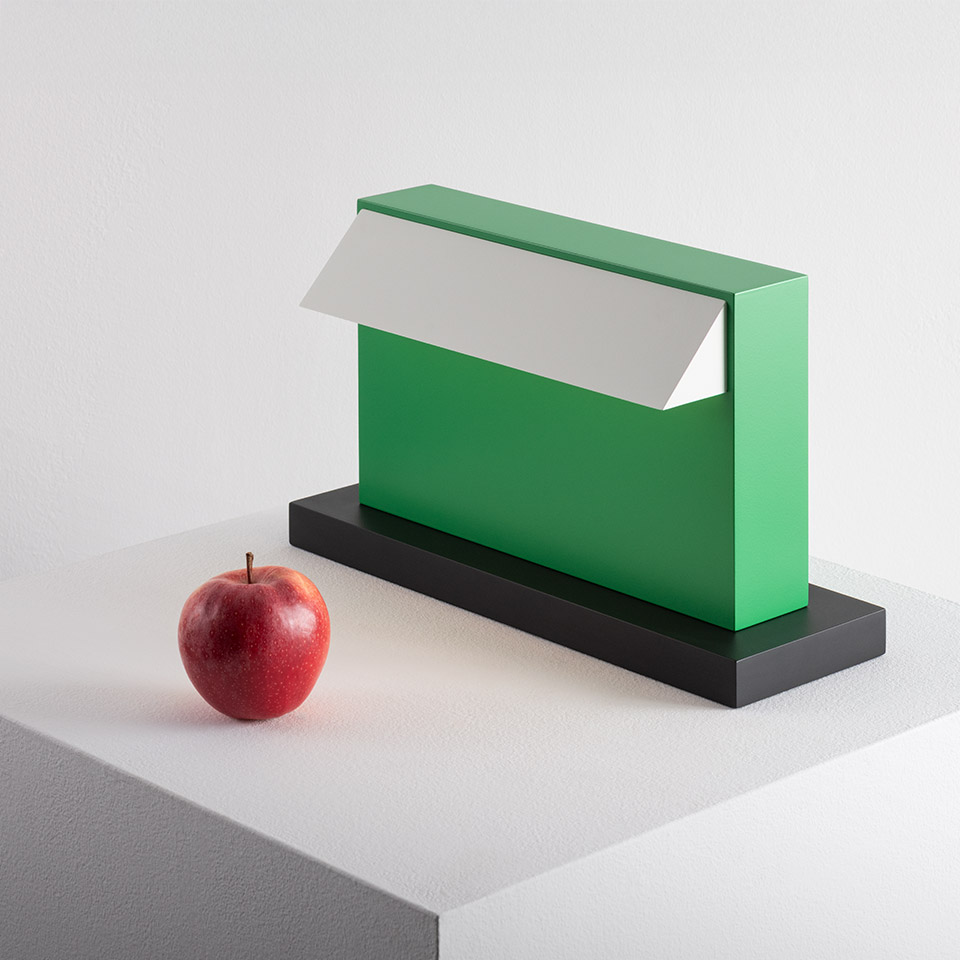 Artemide Hera table lamp in green with white reflector on black base, shown next to a red apple for scale