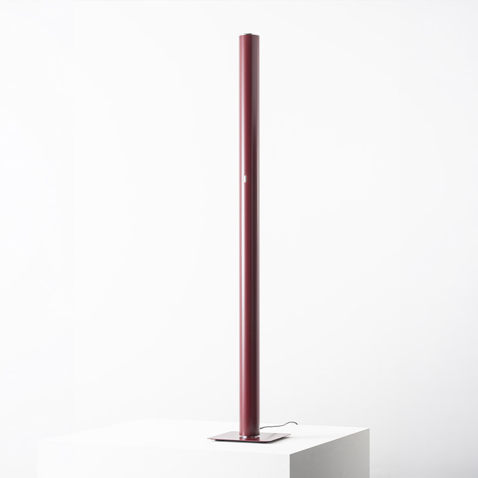 Artemide Ilio floor lamp: tall slim burgundy cylindrical tube on a square flat base, emitting indirect ambient light