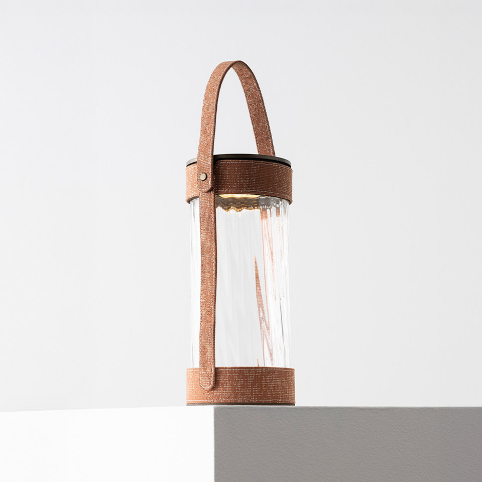 Artemide Laya portable lamp: cylindrical ribbed glass diffuser with warm LED light, held by a brown leather strap handle