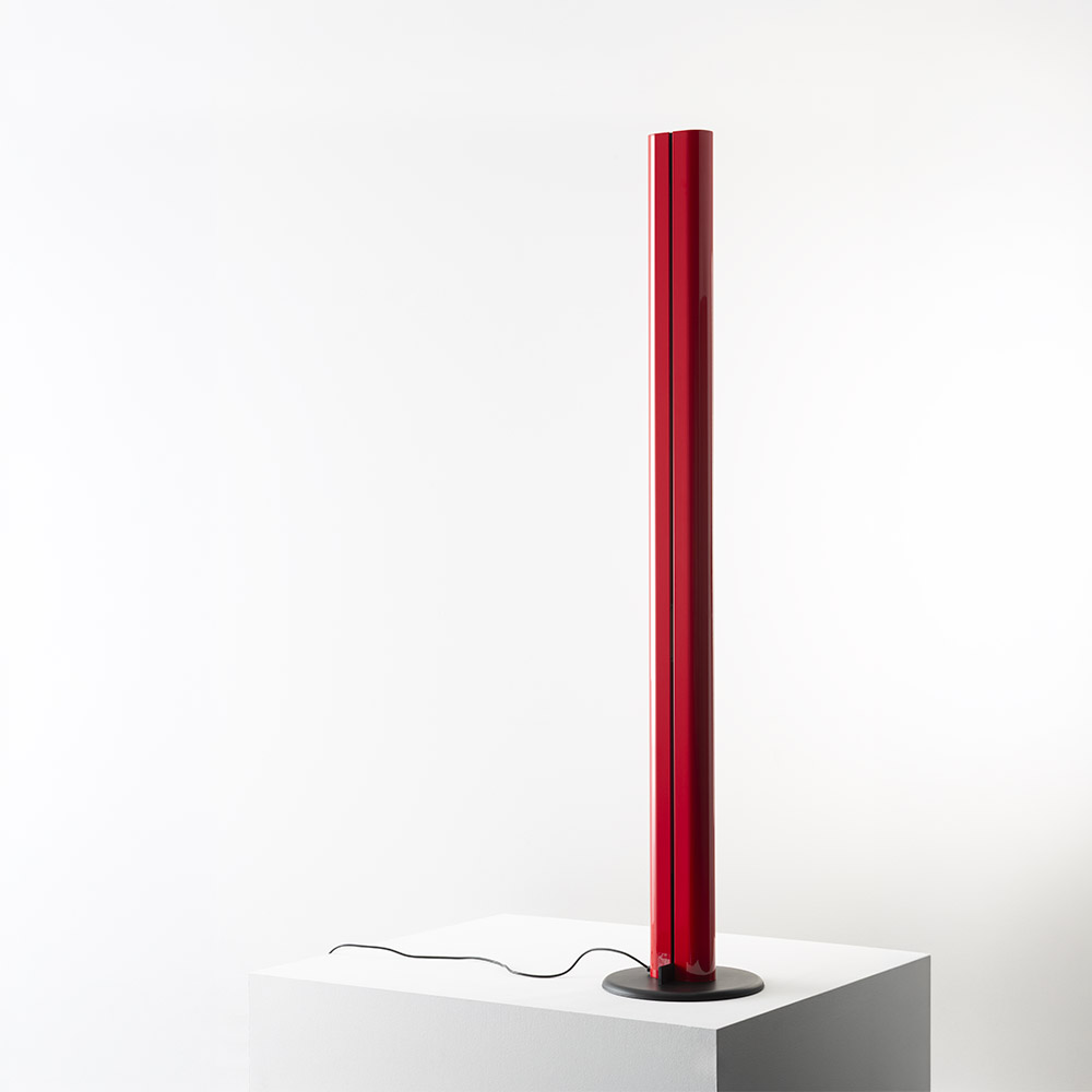 Artemide Megaron floor lamp: tall slim red cylindrical diffuser emitting warm light, mounted on a round black base