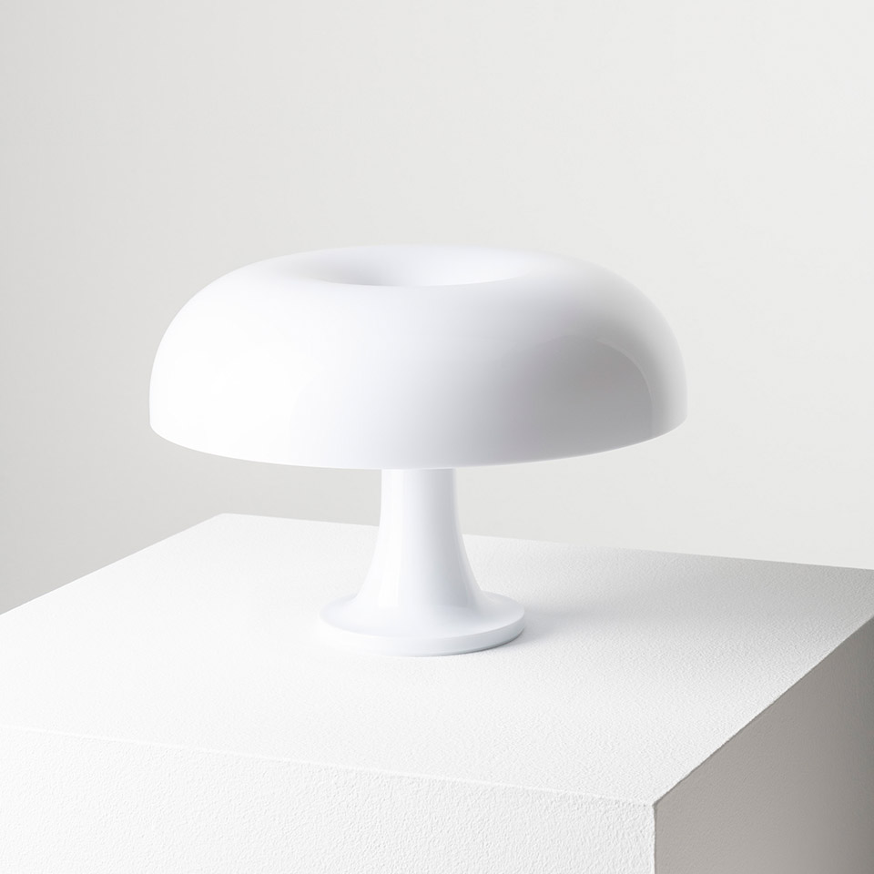 Artemide Nessino table lamp in white, featuring a rounded mushroom-shaped diffuser on a pedestal base, emitting soft ambient light