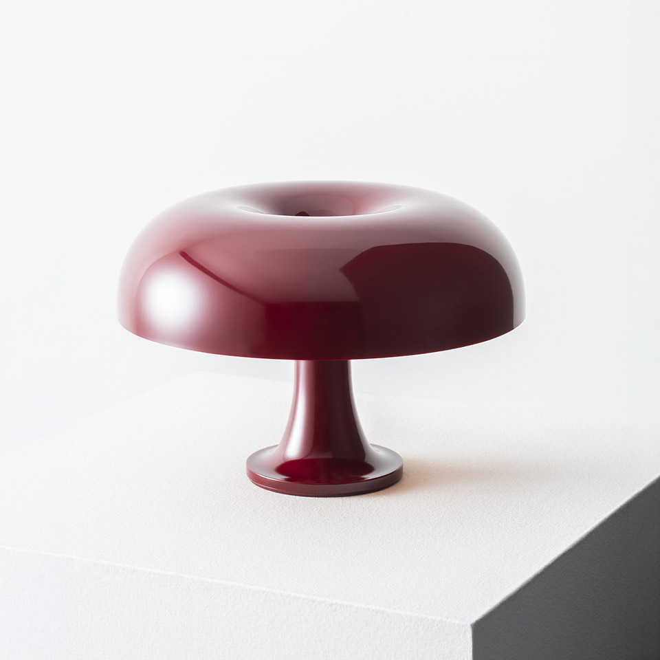 Artemide Nessino table lamp in burgundy red, featuring a glossy donut-shaped shade on a slender pedestal base