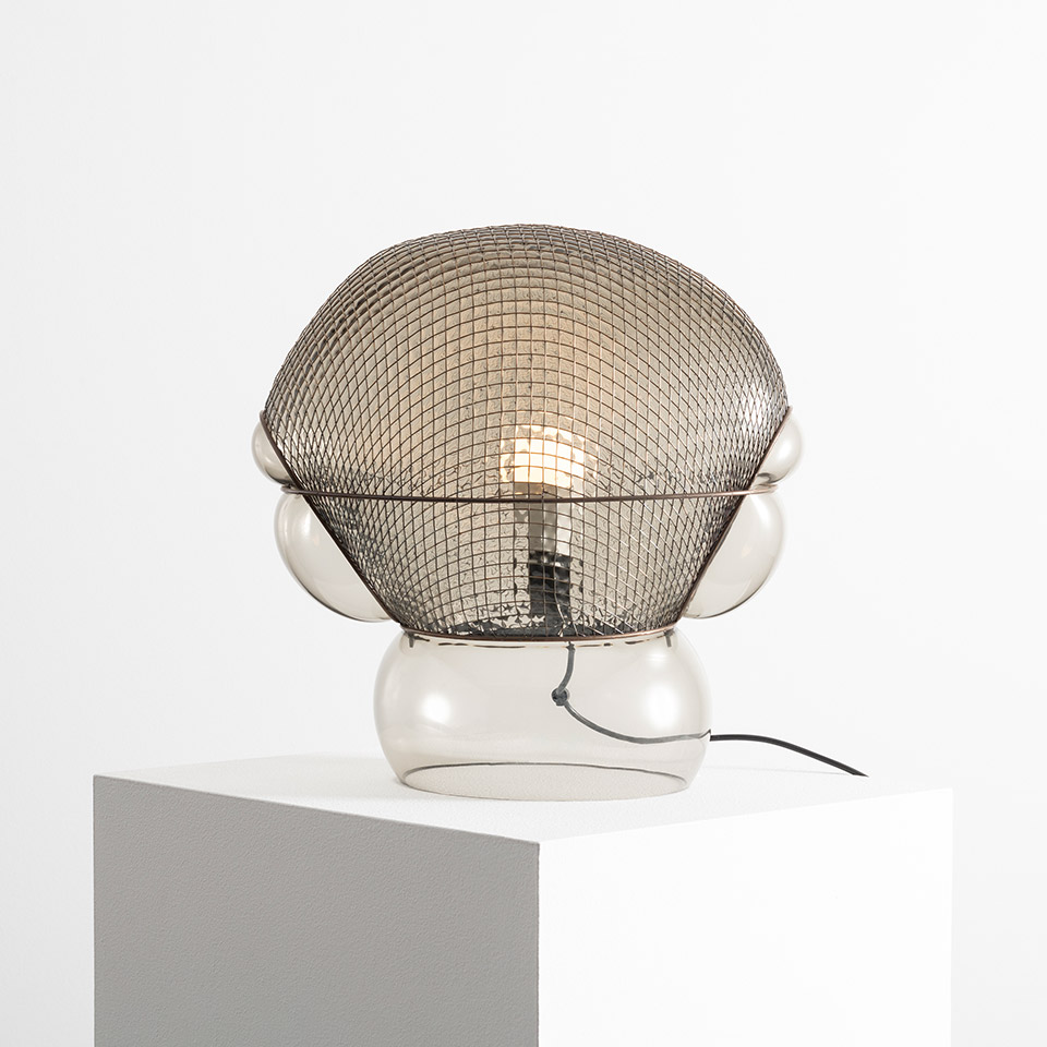 Artemide Patroclo table lamp: transparent glass bubble base with spherical metal mesh shade, exposed filament bulb visible inside
