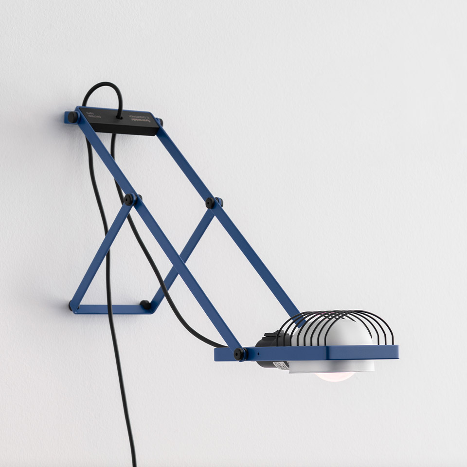Sintesi wall lamp in blue with scissor-arm mechanism, wire cage shade, and exposed black cord, mounted on white wall
