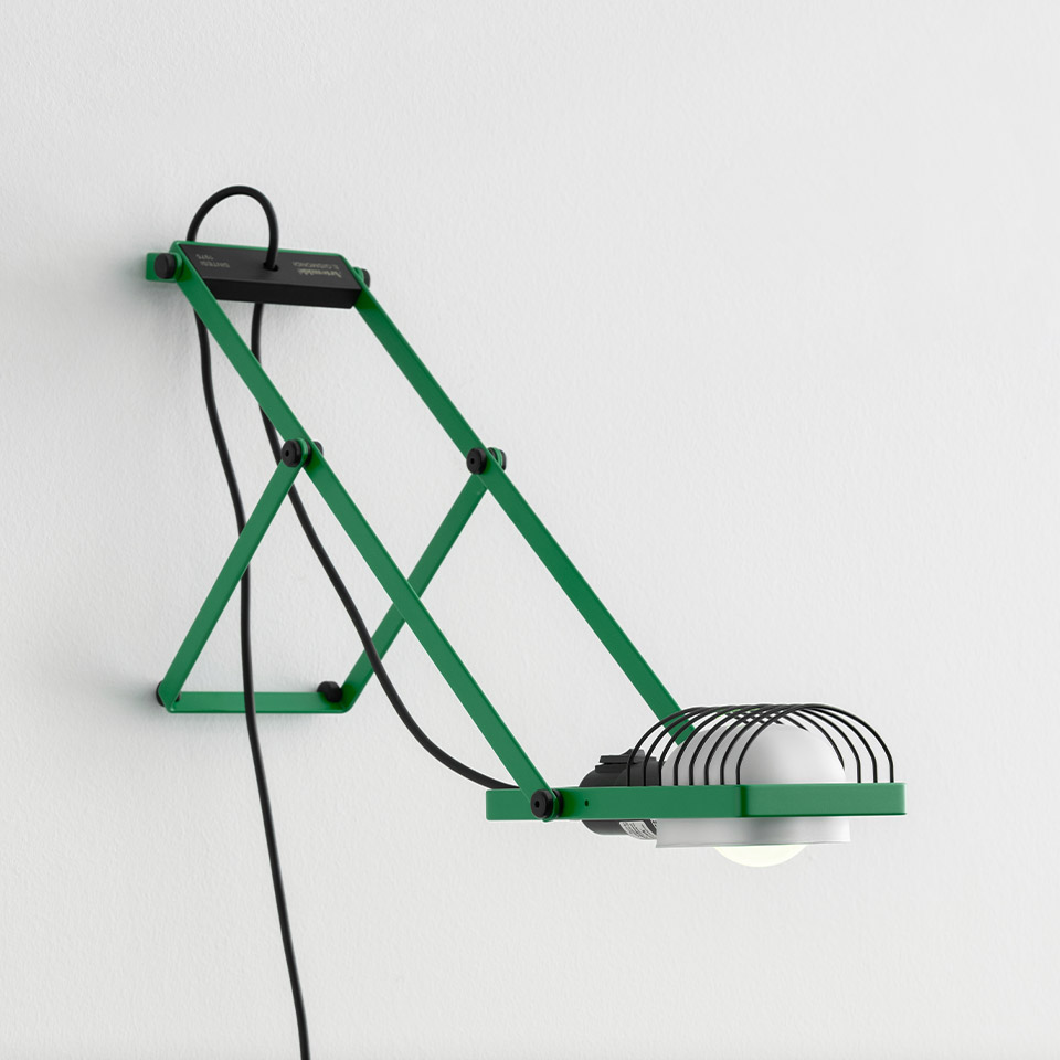 Sintesi wall lamp by Artemide: green scissor-arm structure with wire grid shade, exposed bulb, and black cord on white wall