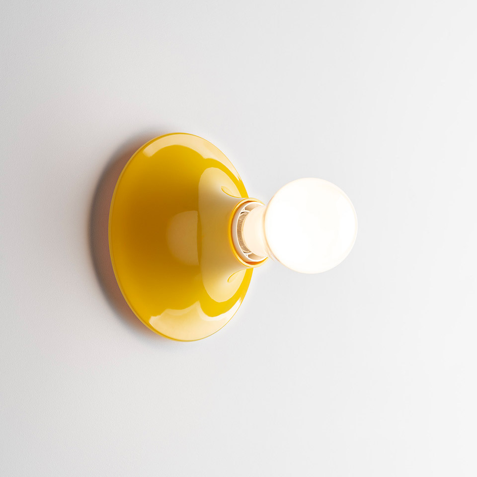Artemide Teti wall lamp with glossy yellow dome-shaped base and exposed spherical frosted bulb mounted on white wall