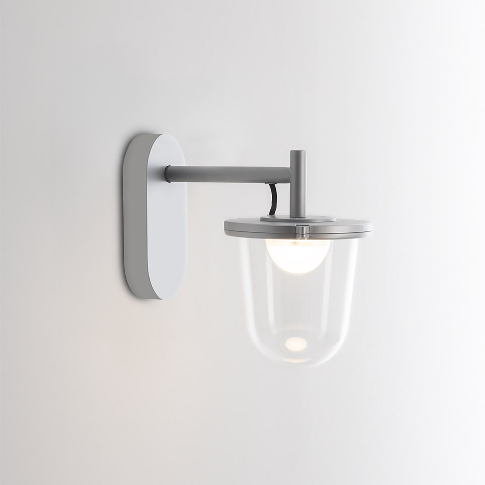 Artemide Tolomeo Outdoor wall lamp: grey metal arm on white backplate, clear glass bell shade with opal bulb visible inside