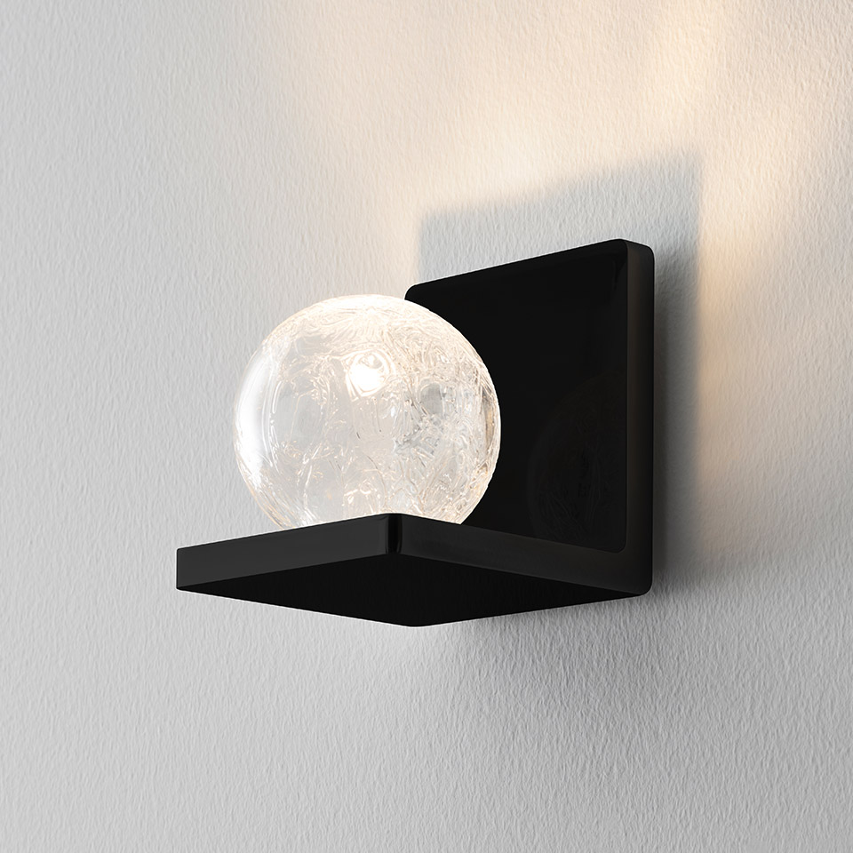 Artemide Ulrich und Diotima wall sconce: matte black square bracket holding a clear crackled glass sphere emitting warm light