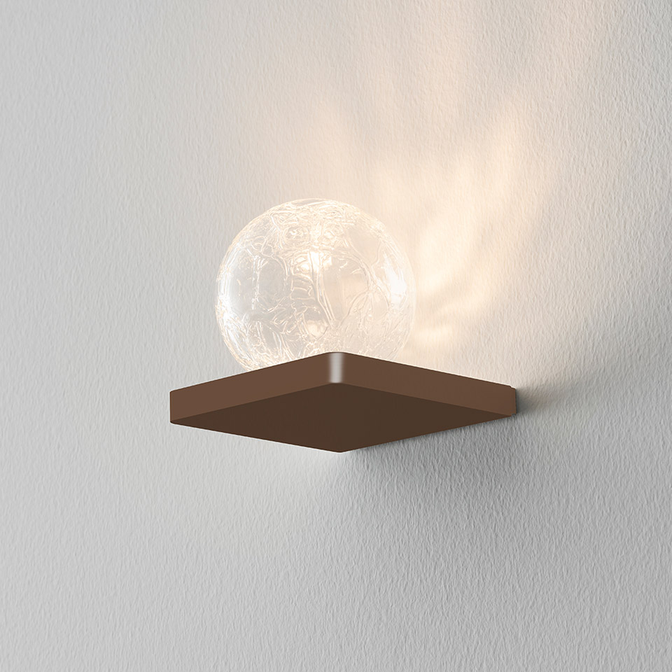 Artemide Ulrich und Diotima wall lamp: bronze square base with crackled glass sphere emitting warm light on white wall