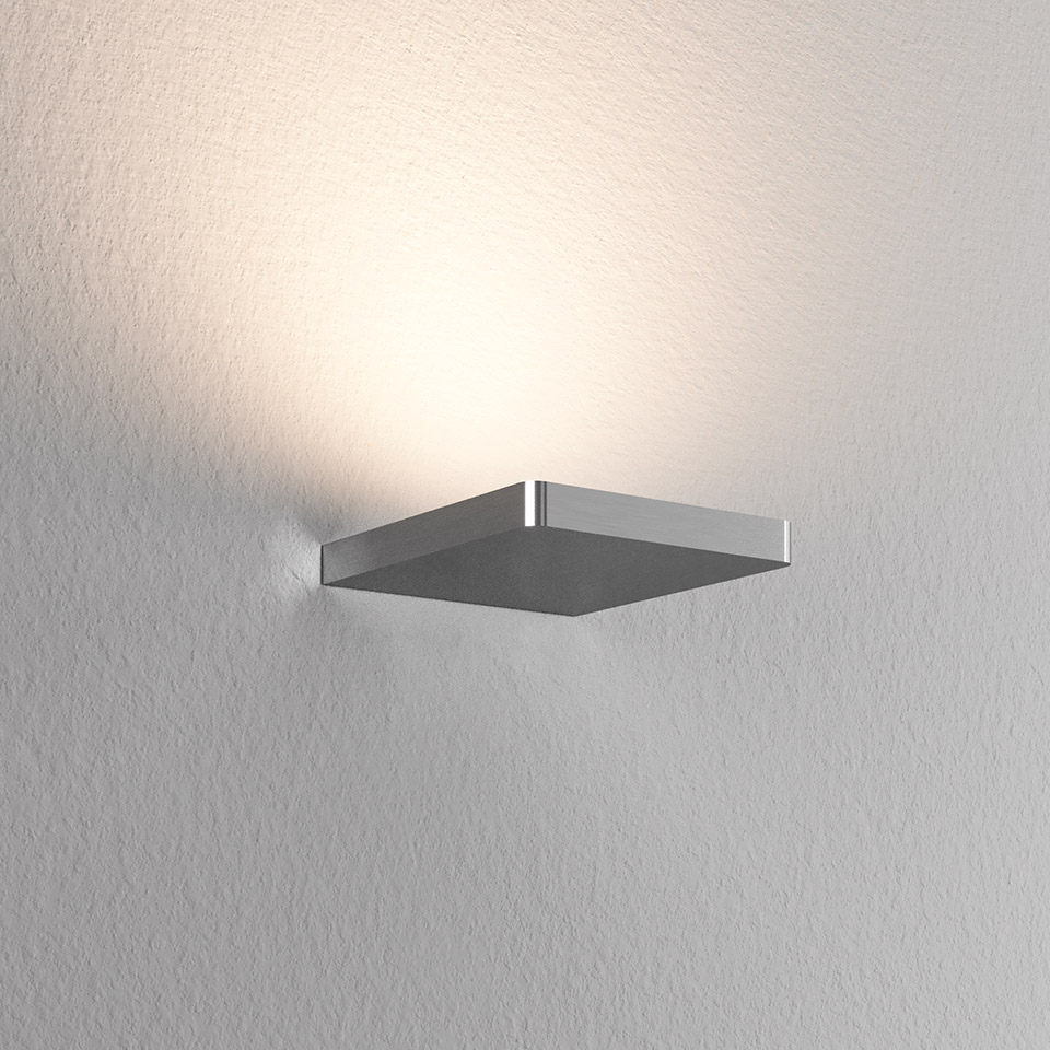 Artemide Ulrich und Diotima square wall lamp in chrome, emitting warm upward light against a textured white wall