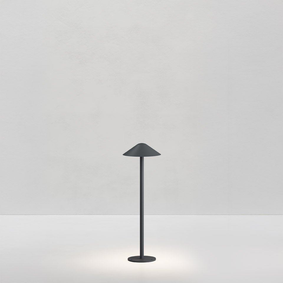 Artemide Vea Bollard table lamp in dark grey, slim stem with conical shade, emitting soft downward light on a white background