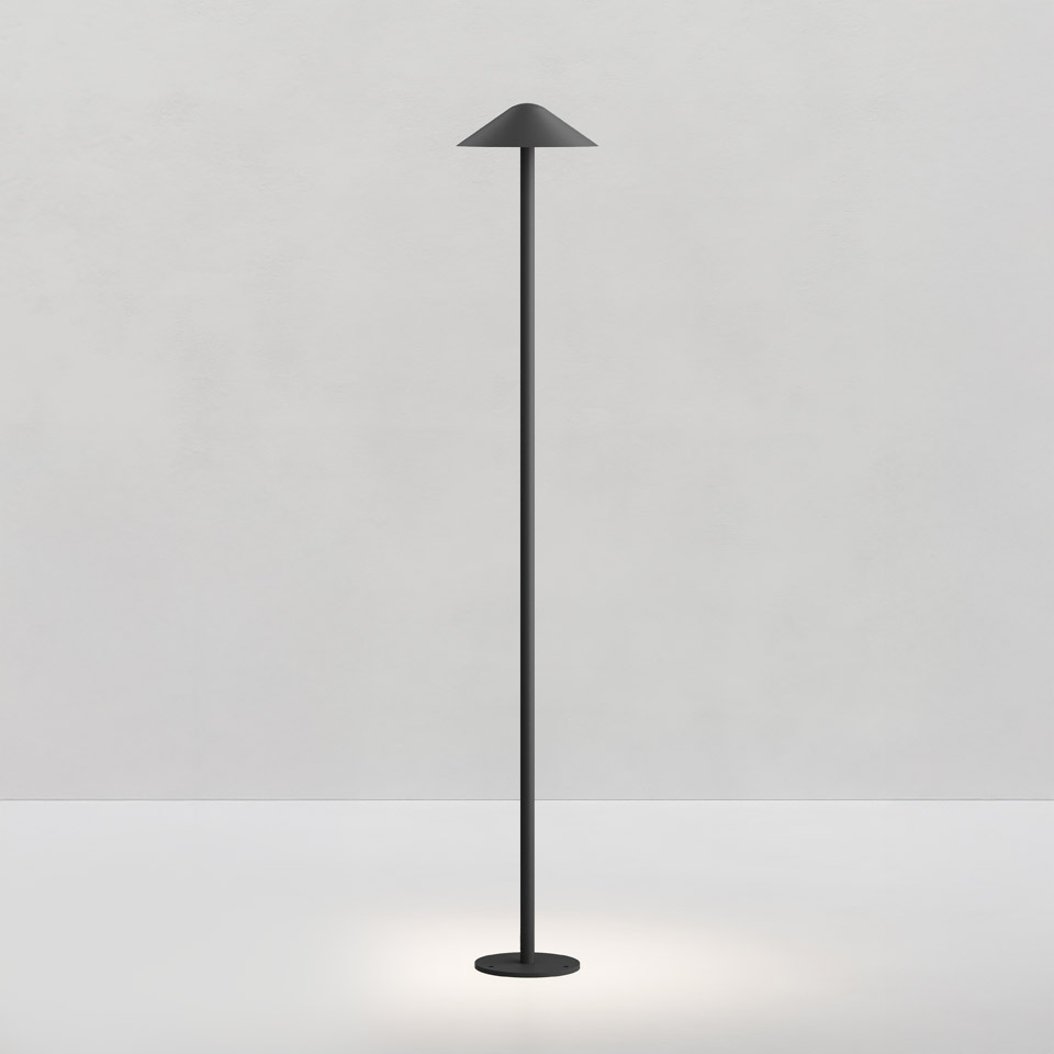 Artemide Vea floor lamp in matte black, featuring a slender stem, conical shade, and circular base emitting soft downward light