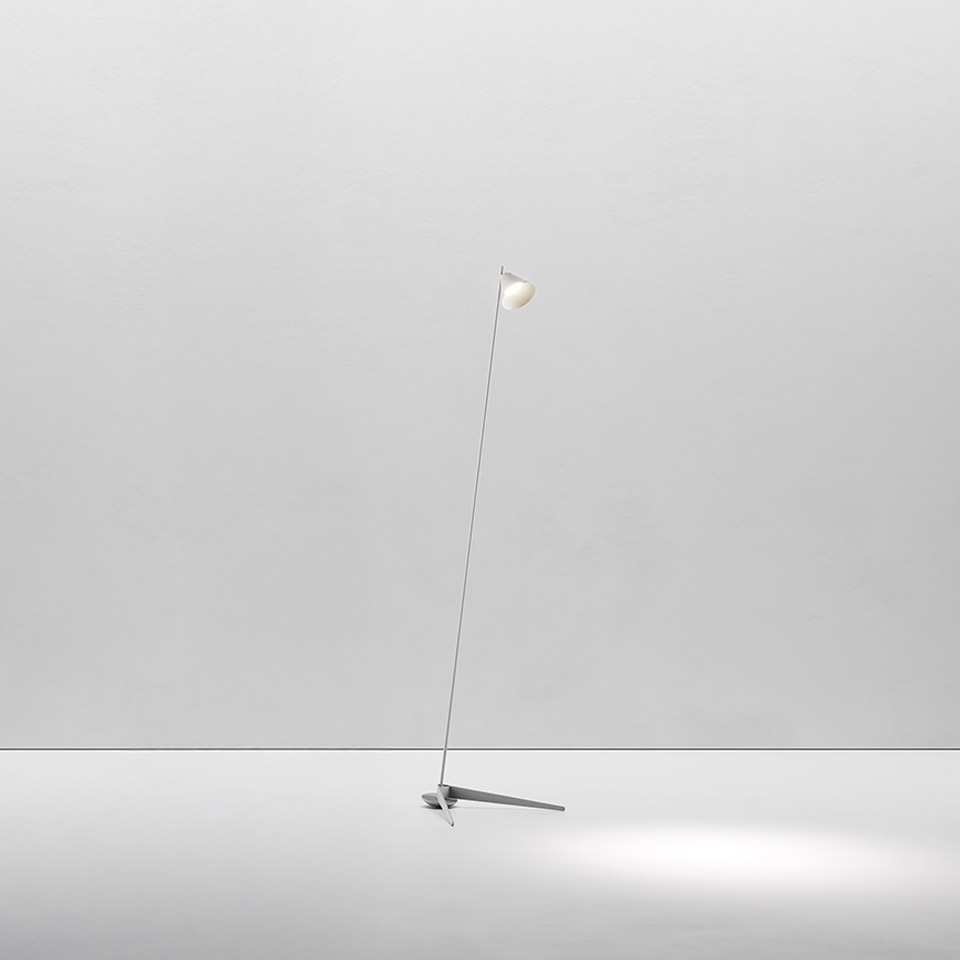 Artemide Vea floor lamp: slender angled stem with small spherical white diffuser on a minimal three-pronged base, casting soft downward light