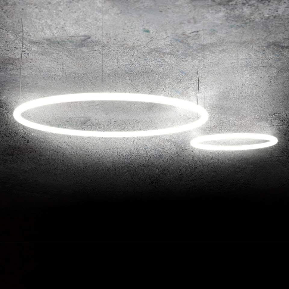Two Artemide Alphabet of Light Circular LED ring pendants mounted at angles on a concrete ceiling, one large and one small