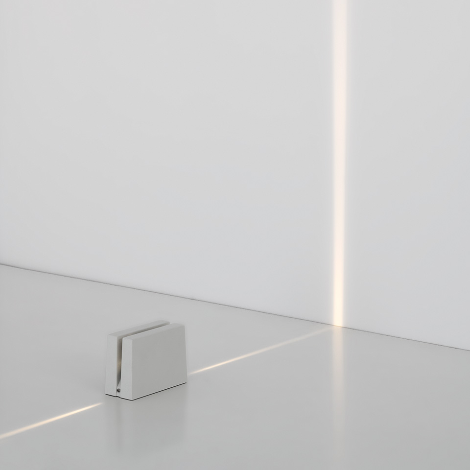 Antarktikós floor lamp by Artemide: compact white cube emitting a precise vertical beam of light along a white wall corner