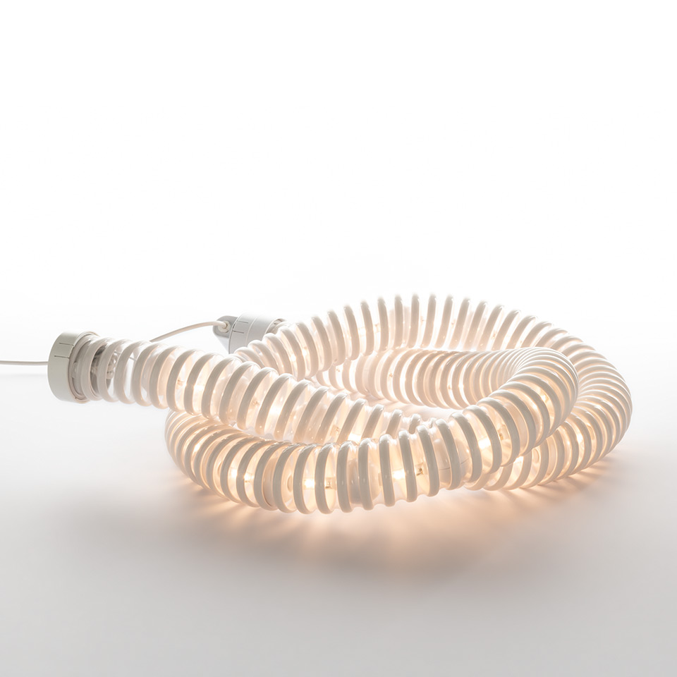 Artemide Boalum lamp: flexible luminous white tube coiled in a spiral on a surface, emitting warm diffused light