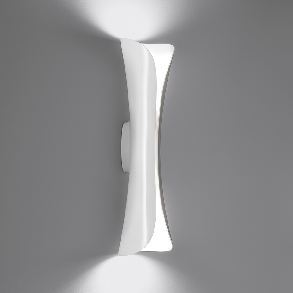 Artemide Cadmo wall lamp in white, hourglass-shaped diffuser emitting upward and downward light beams against a grey wall