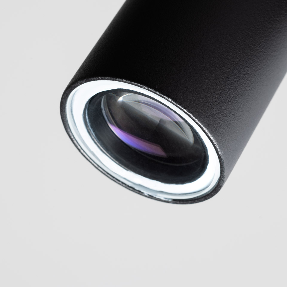 Close-up of Artemide Coherence spotlight: black cylindrical body with precision optical lens, featuring anti-reflective coating.