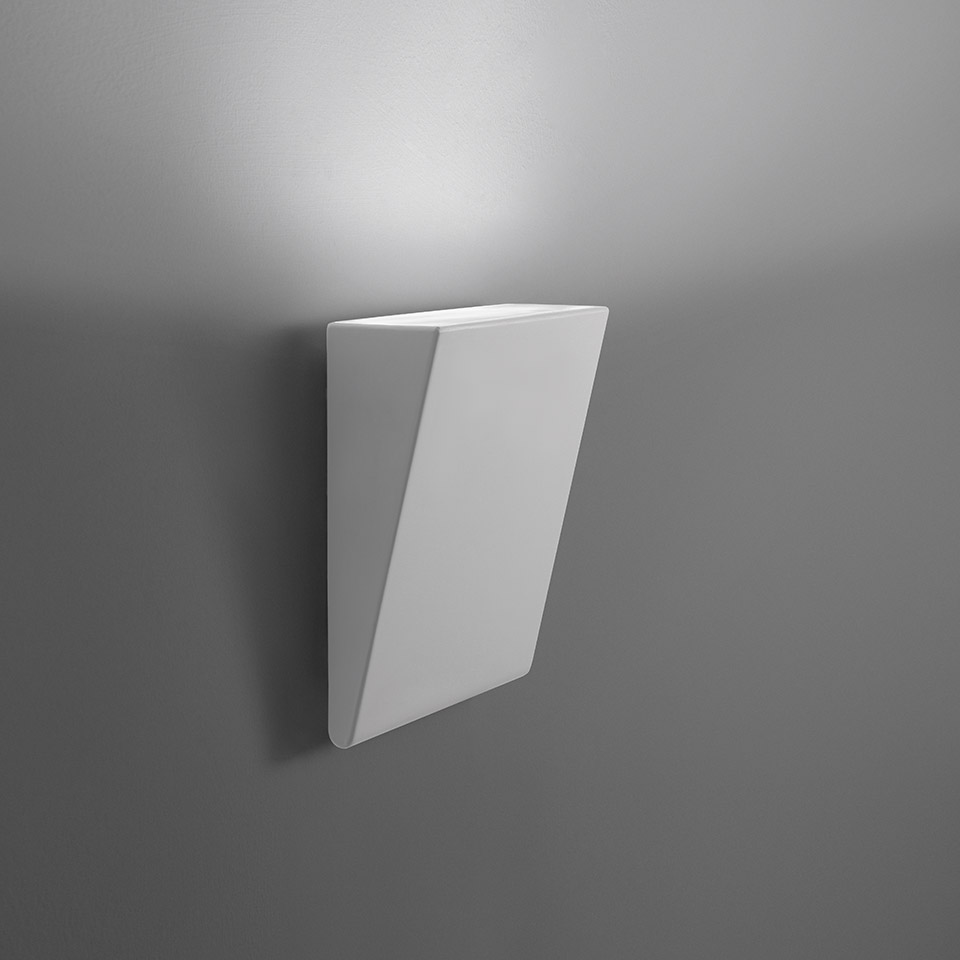 Artemide Cuneo wall lamp, white angular geometric body emitting upward indirect light against a grey wall