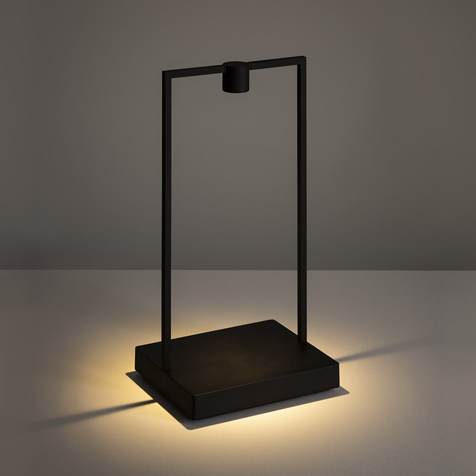 Artemide Curiosity table lamp: minimalist black rectangular frame with suspended LED light source, warm glow emanating from square base