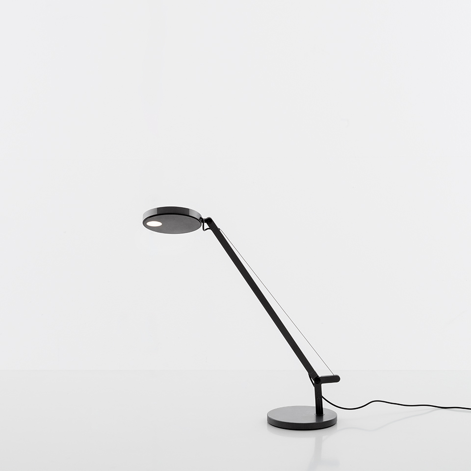 Artemide Demetra Micro table lamp in black, featuring a circular disc head, angled arm with tension wire, and round base.