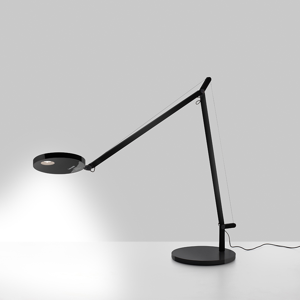 Artemide Demetra table lamp in black, featuring an adjustable arm, circular LED head, and round base casting focused light.