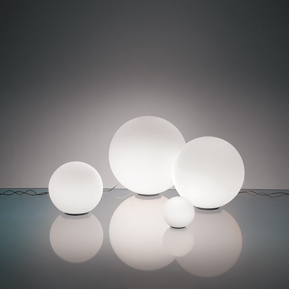 Four Artemide Dioscuri table lamps in varying sizes, featuring frosted white spherical glass diffusers resting on a reflective surface