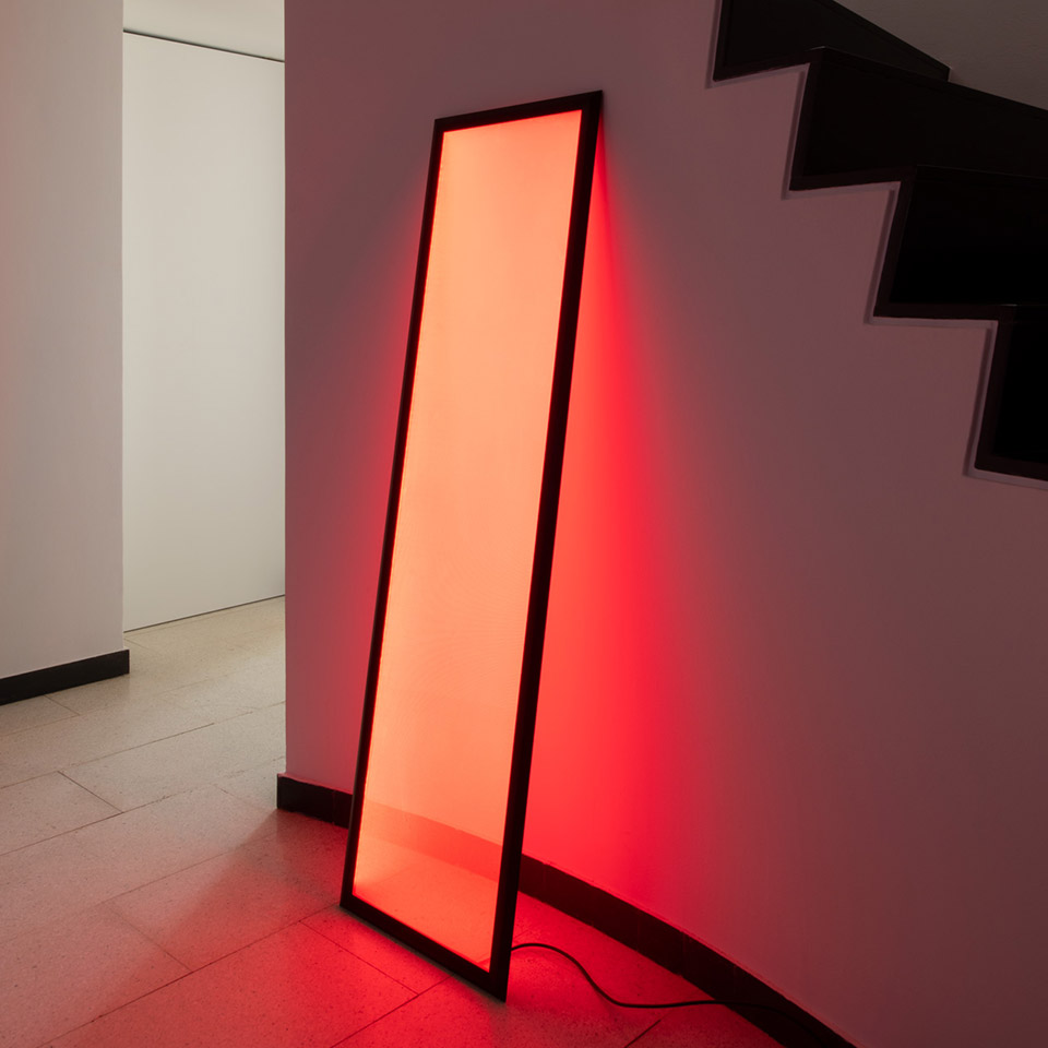 Artemide Discovery Terra floor lamp with black frame leaning against wall, emitting vibrant red light, illuminating staircase area