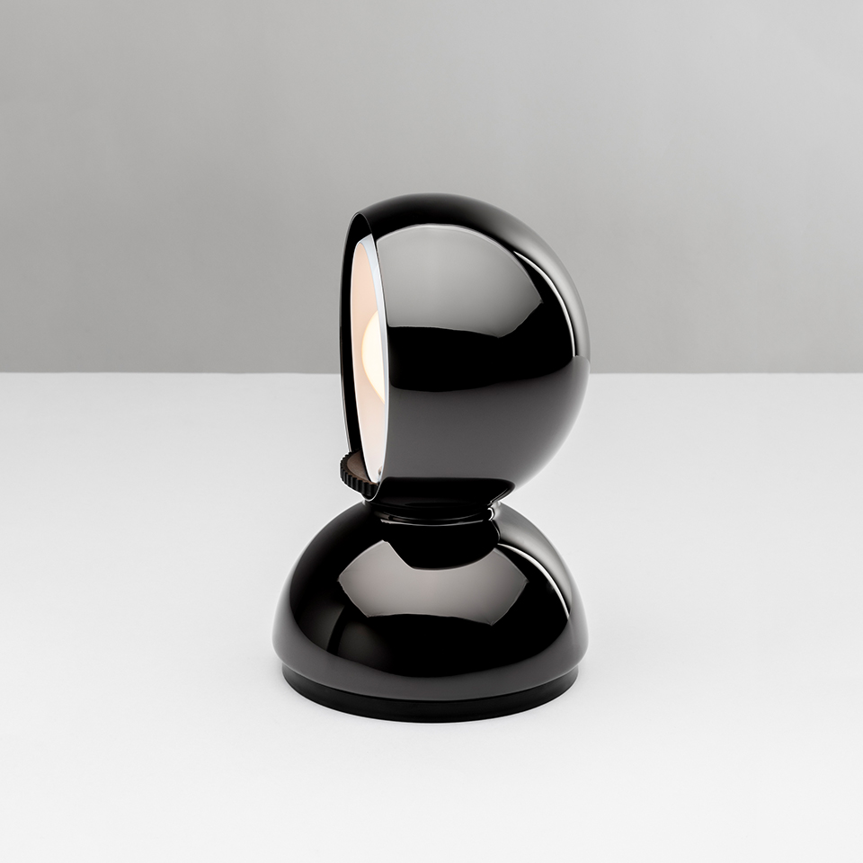 Artemide Eclisse table lamp in glossy black, featuring a spherical rotating shade on a dome-shaped base, partially open to reveal warm light