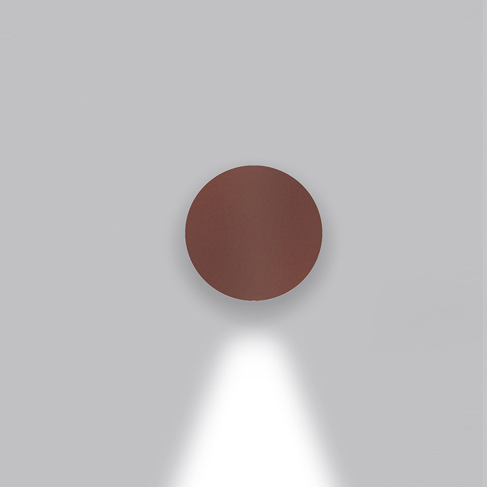 Artemide Effetto wall lamp in burgundy red, circular disc shape, emitting a downward cone of white light on a grey wall