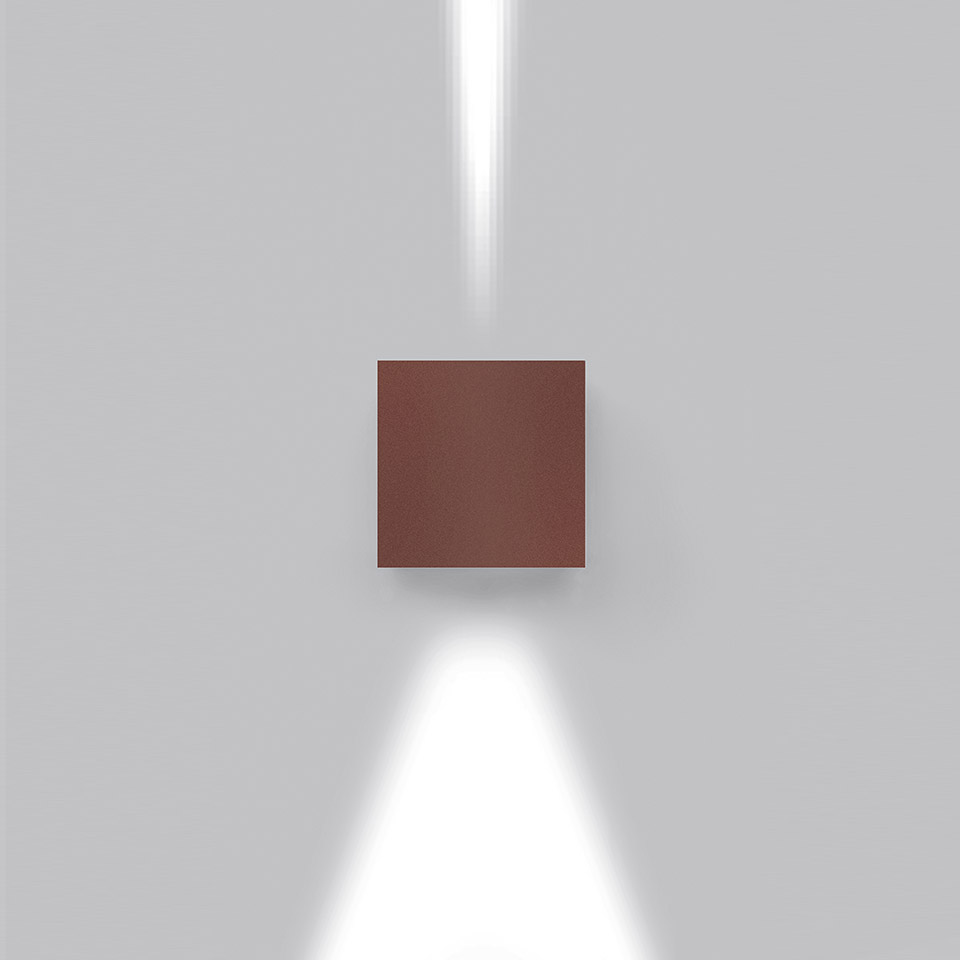 Effetto wall lamp in brown-red finish, emitting two narrow beams of white light upward and downward on a grey wall