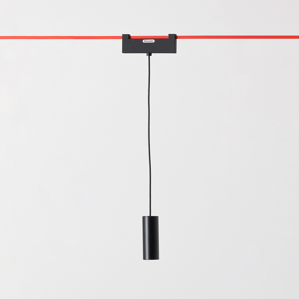 Artemide Funivia black pendant lamp with cylindrical shade hanging from a track adapter on a red cable rail system
