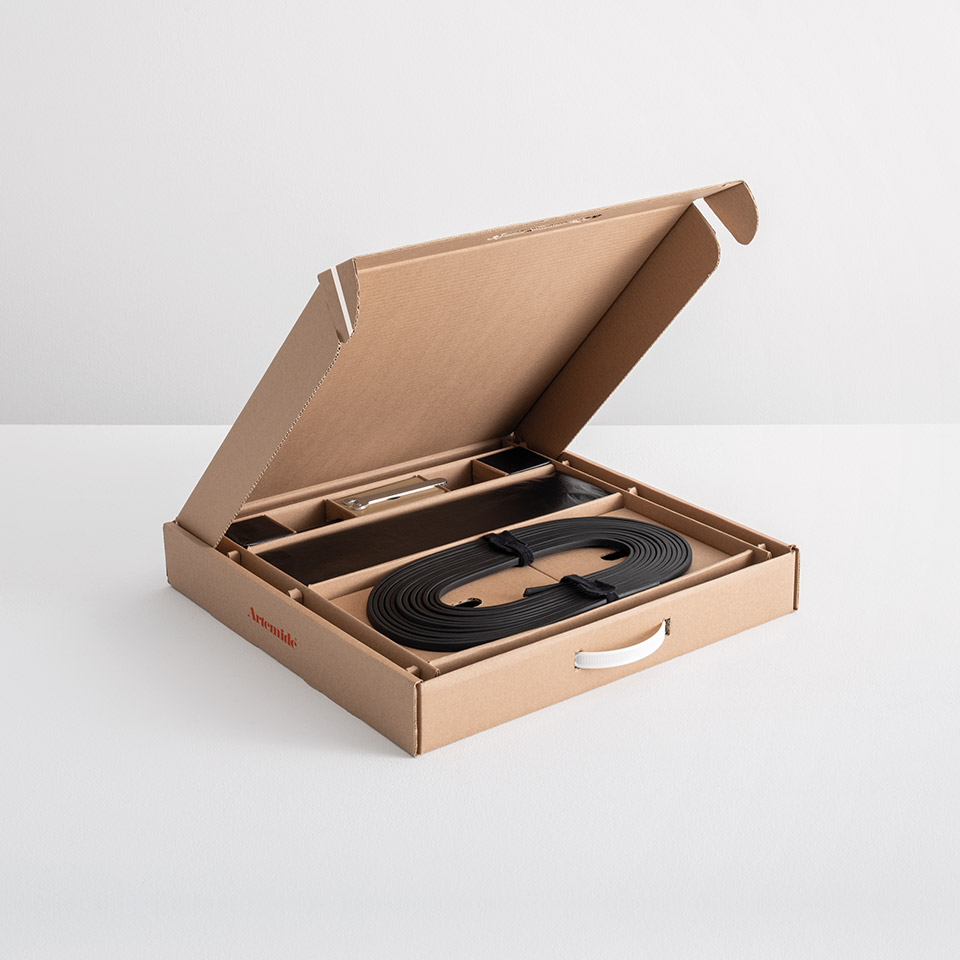 Artemide Funivia lighting system unboxed: open cardboard box revealing coiled black flat cable, mounting hardware, and components