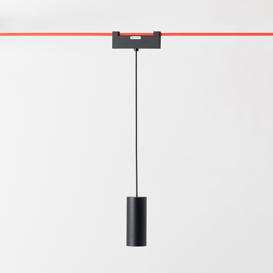 Artemide Funivia: black cylindrical pendant lamp suspended on a thin cable from a black adapter mounted on a red track system