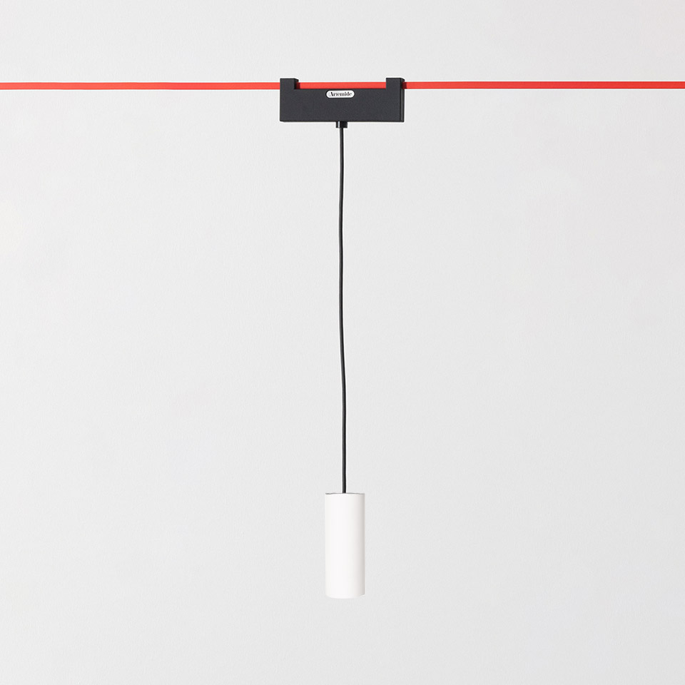 Artemide Funivia pendant lamp: white cylindrical fixture hanging from black cable attached to red overhead track system