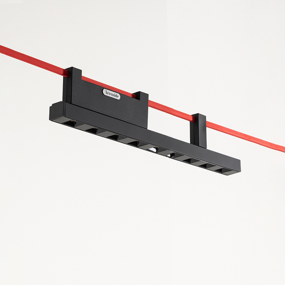 Artemide Funivia black linear LED track light mounted on a red cable suspension system against a white ceiling