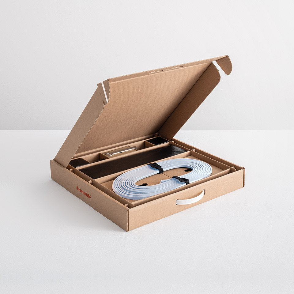 Artemide Funivia lighting system unboxed: open cardboard box revealing coiled flat cable and mounting components neatly organized