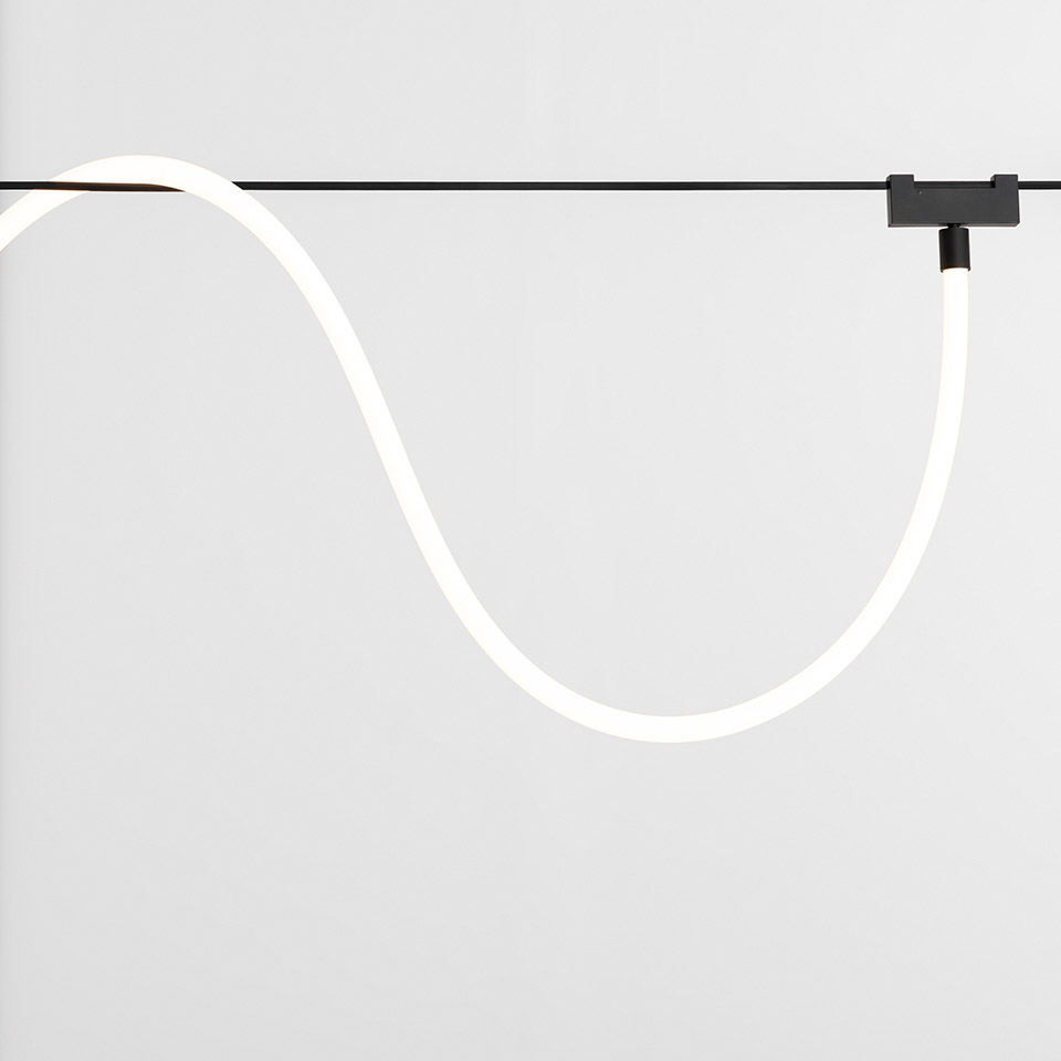 Artemide Funivia: flexible white LED light tube suspended from a black cable track system, forming an elegant S-curve