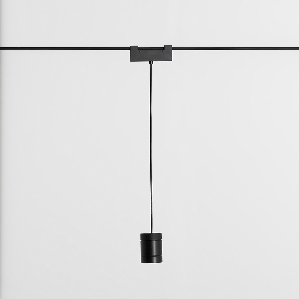 Artemide Funivia black pendant lamp suspended from a track rail via a thin cable, featuring a compact cylindrical black fixture