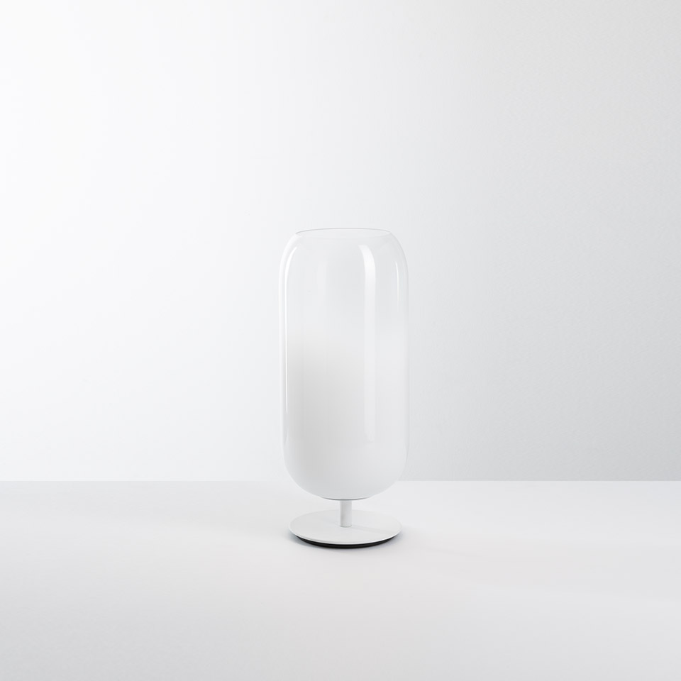 Artemide Gople table lamp: tall oval white blown glass diffuser on a small round white base, emitting soft ambient light