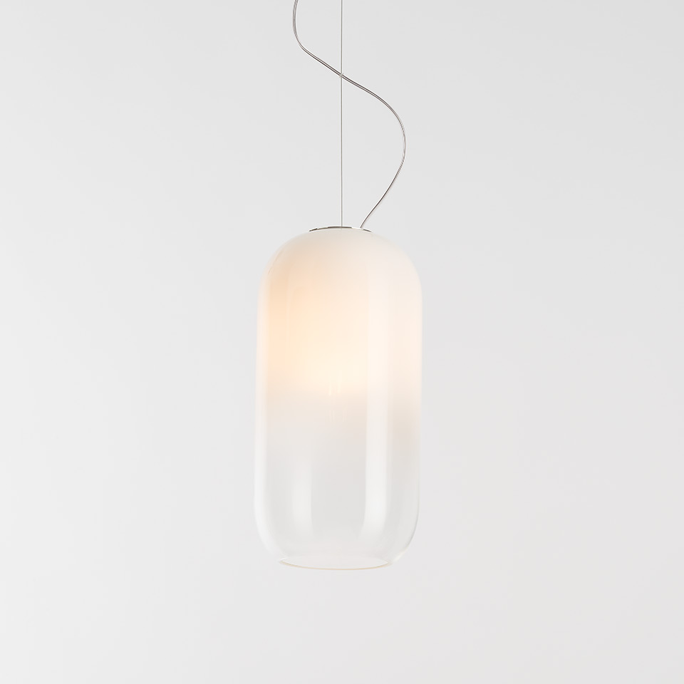 Artemide Gople pendant lamp: elongated capsule-shaped frosted white glass diffuser, warm glow at top, suspended by thin chrome cable - 2