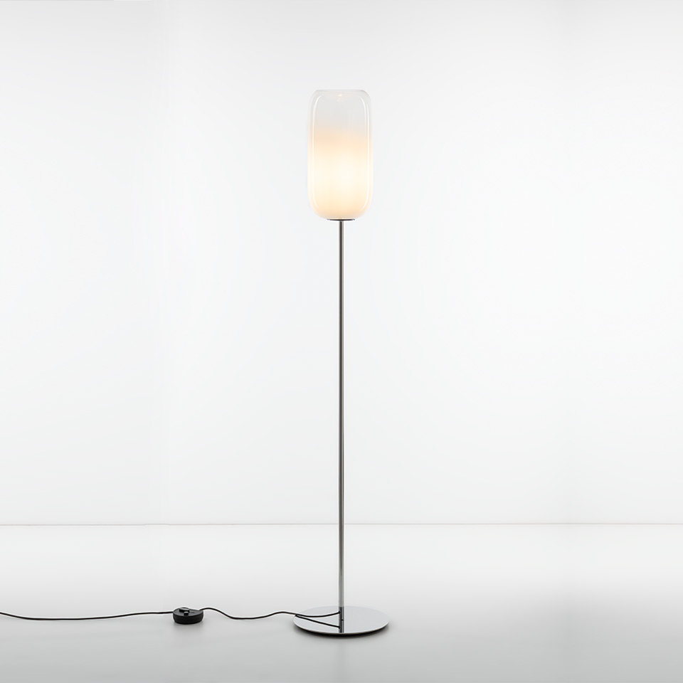 Artemide Gople floor lamp with tall chrome stem, round base, and elongated frosted glass shade glowing softly white