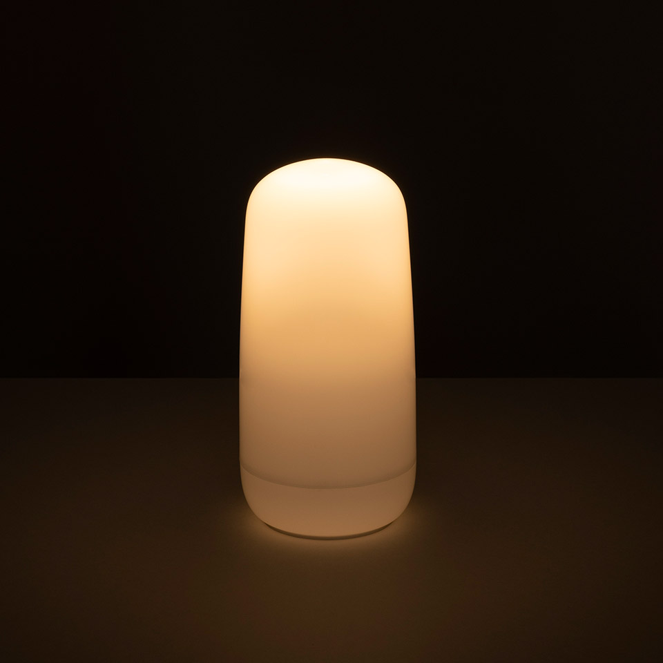 Artemide Gople Portable lamp glowing with warm white light, featuring a smooth rounded cylindrical opal diffuser on a dark surface - 2