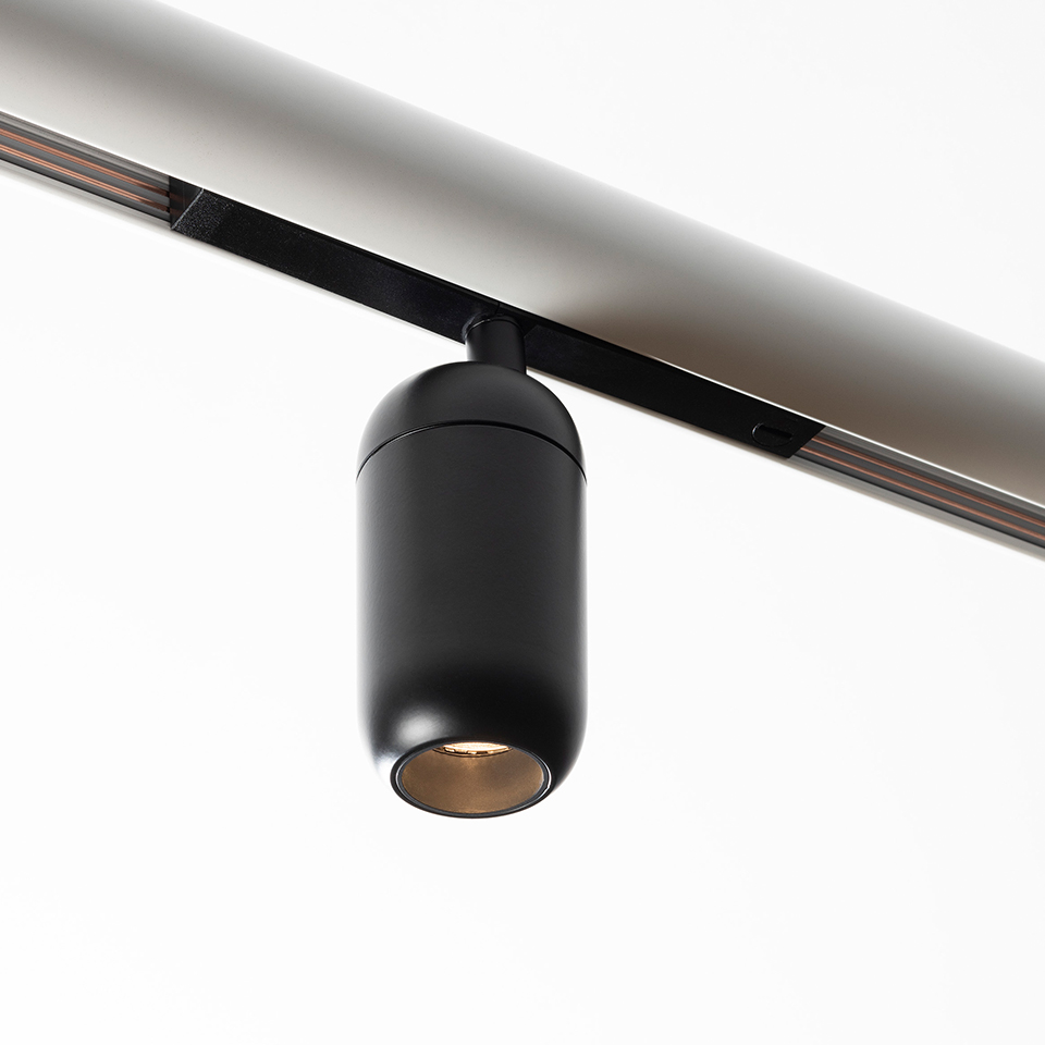 Artemide Gople System: black cylindrical LED track spotlight mounted on a ceiling rail, with warm-toned interior reflector