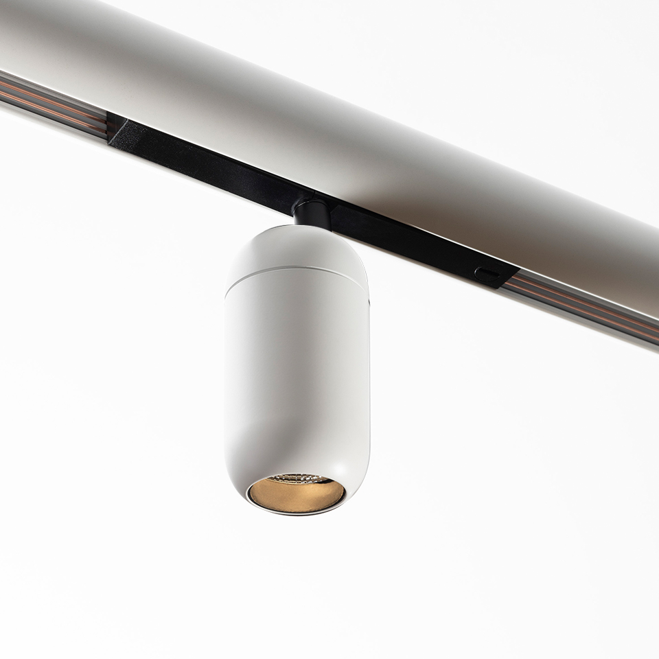 Artemide Gople System track spotlight: white cylindrical LED fixture with gold interior, mounted on a ceiling rail track