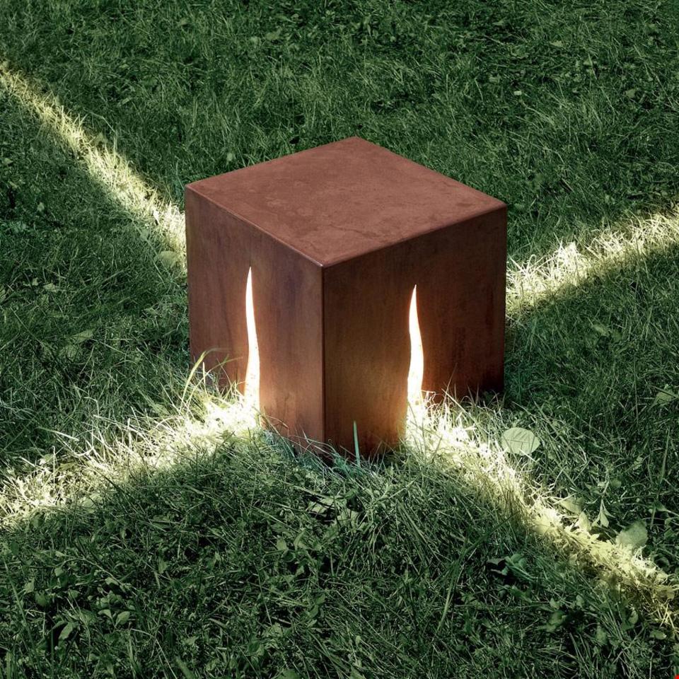 Artemide Granito outdoor floor lamp: Corten steel cube with flame-shaped slits casting dramatic light rays on surrounding grass