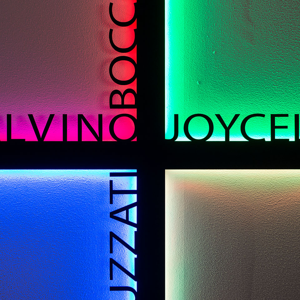 Four illuminated frosted glass panels in a grid, glowing in pink, green, blue, and white, with text fragments: LVINO, OBOCO, JOYCE, UZZATI