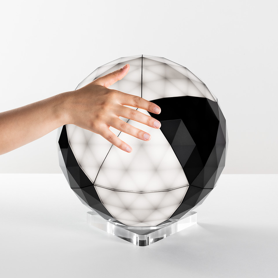 Artemide Huara table lamp: faceted spherical diffuser on crystal base, hand touching its black and white geometric surface