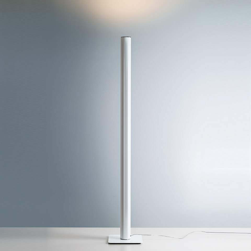 Artemide Ilio floor lamp: slim white cylindrical column on square base, emitting warm upward indirect light