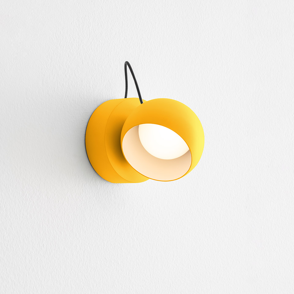 Artemide Ixa wall lamp in yellow, featuring a round rotating shade with a white interior and black cable mount